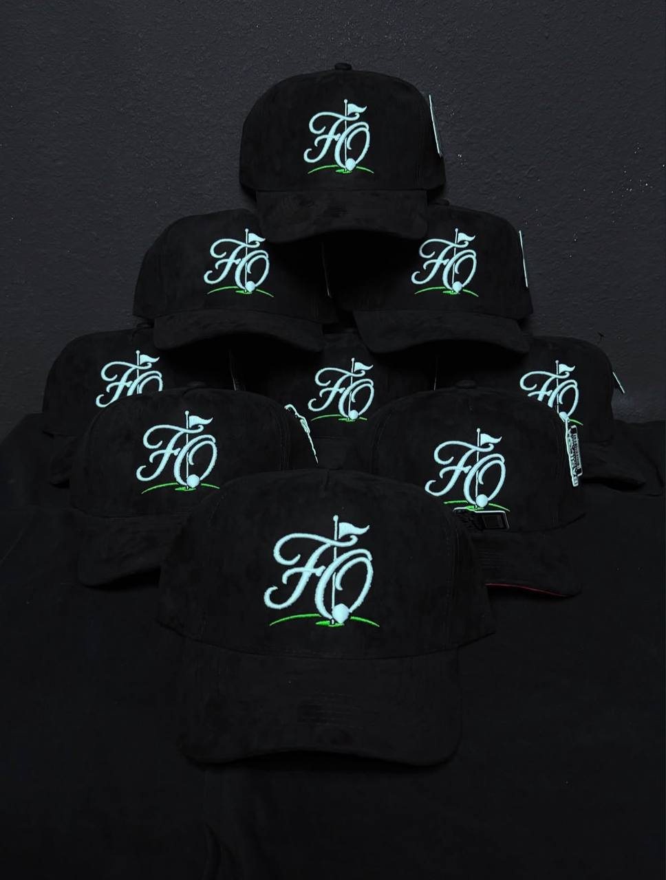 A stack of black hats with the FO golf logo stitched in white and green