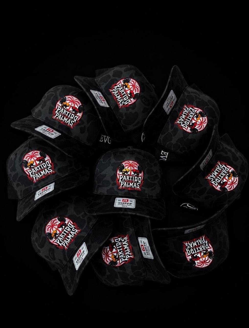 Black camo Richardson caps arranged in a circle, each with the Partido Palmas logo in red, white and gold