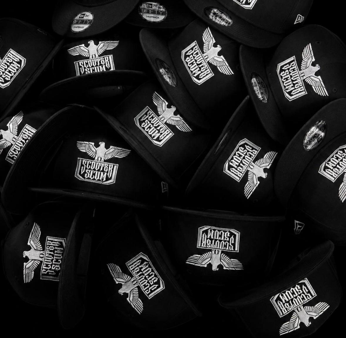 A pile of black New Era snapbacks with the Scouter Scum eagle logo stitched in white