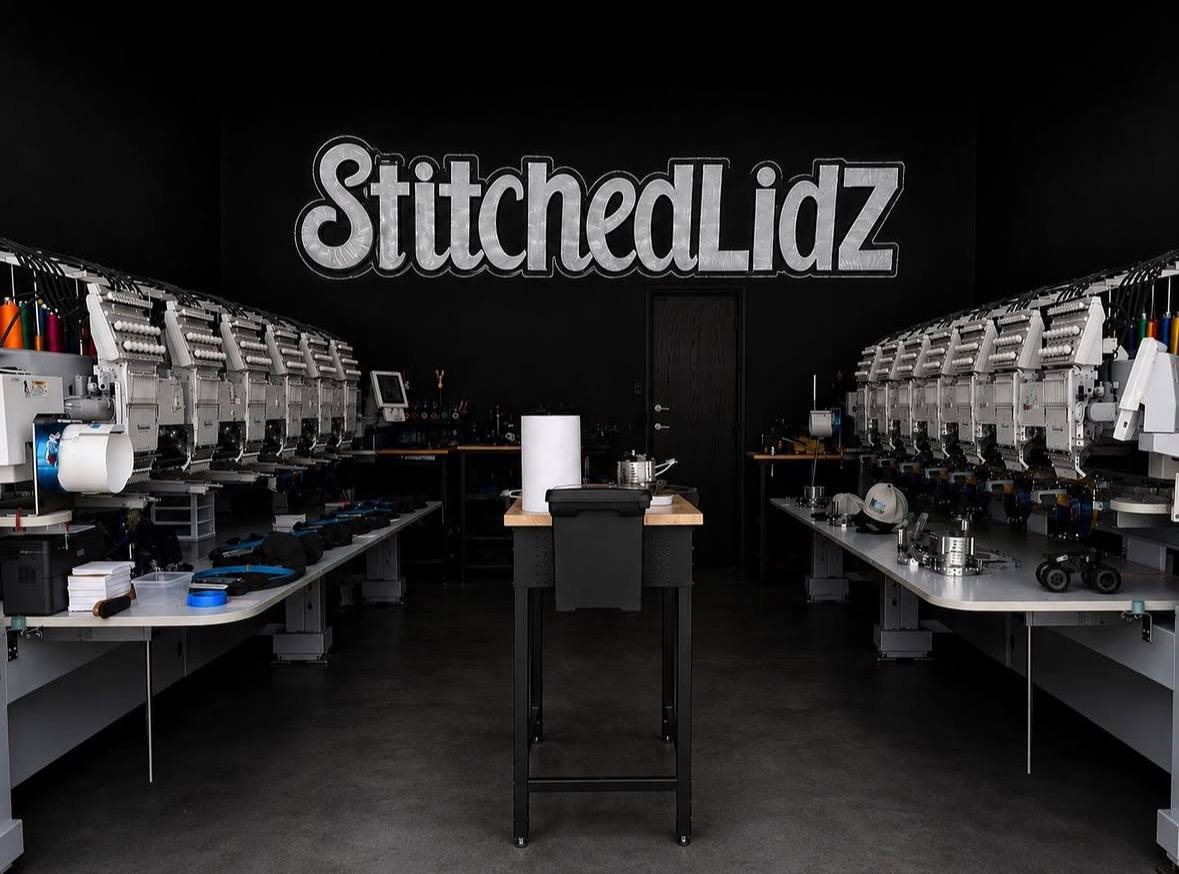 The Stitched Lidz shop: black walls, the Stitched Lidz sign, and rows of embroidery machines on both sides